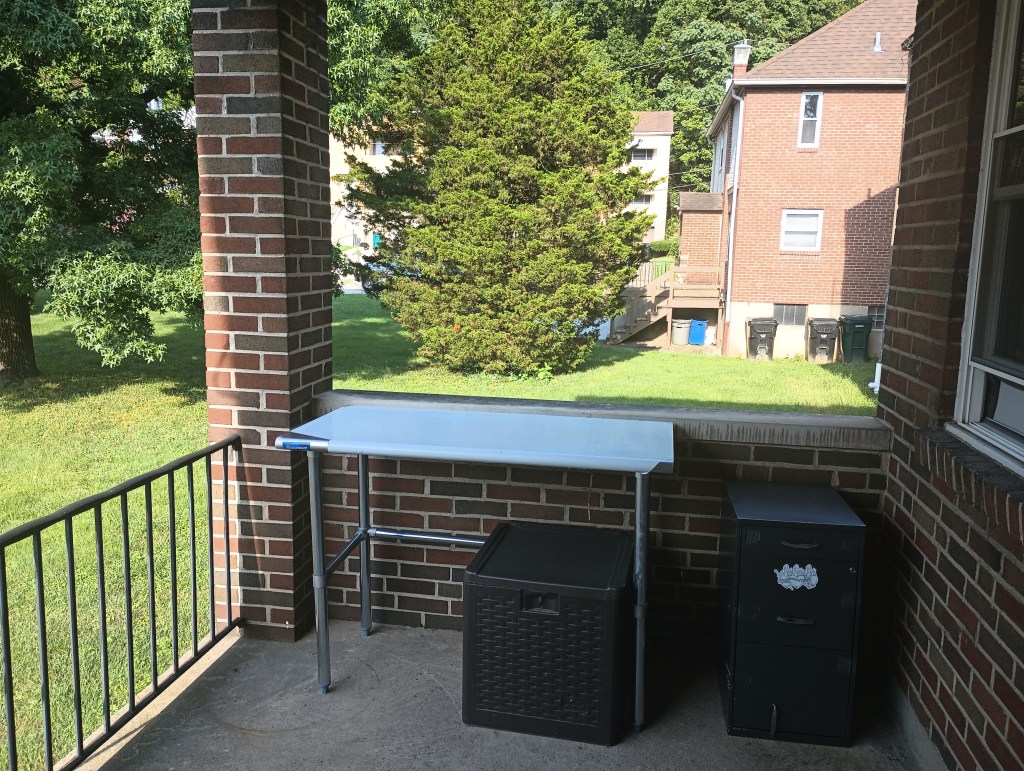 Initial furniture placement on the balcony features a stainless steel table, a small, square lock box, and a filing cabinet with a Sacred Hearts magnet and a broken bottom drawer handle.