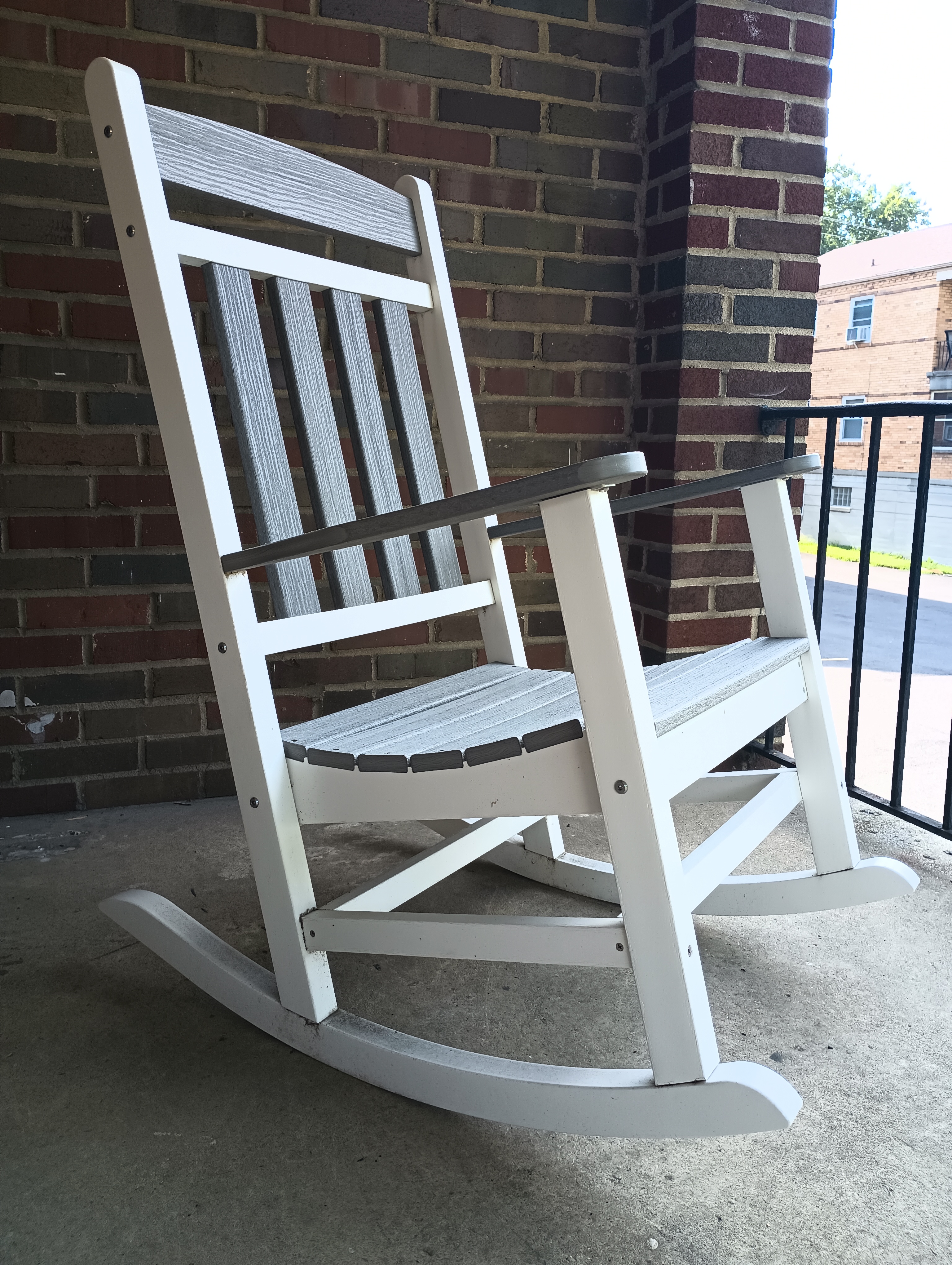 Closeup of white rocking chair with grey detailing. The chair is on a concrete and brick balcony overlooking the view.
