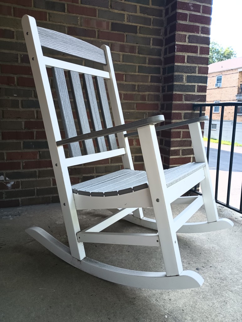 Closeup of white rocking chair with grey detailing. The chair is on a concrete and brick balcony overlooking the view.