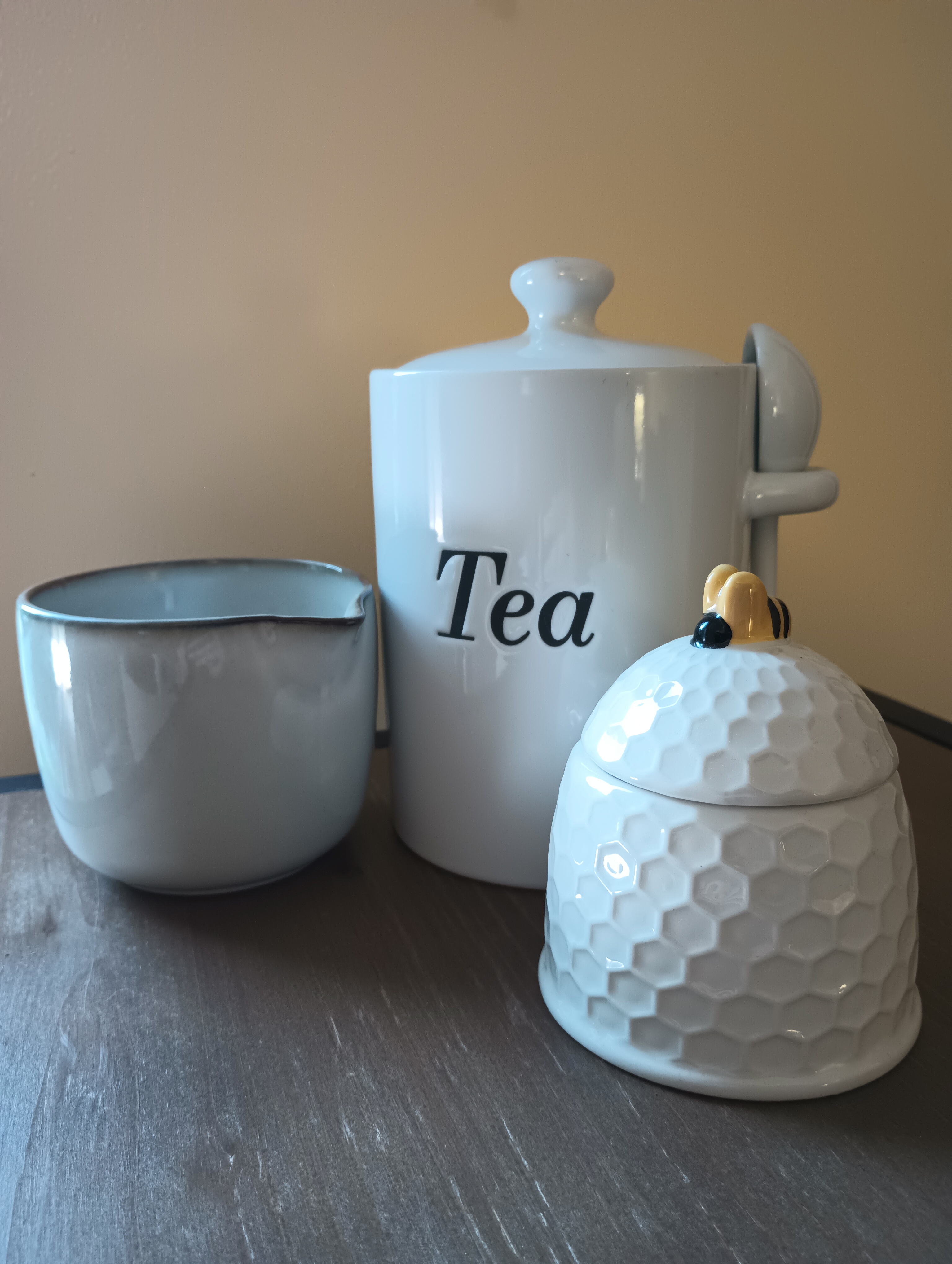 Closeup of ceramic tea accessories - a loose-leaf jar and spoon for tea, a creamer pot, and a hive-shaped jar to hold sugar.